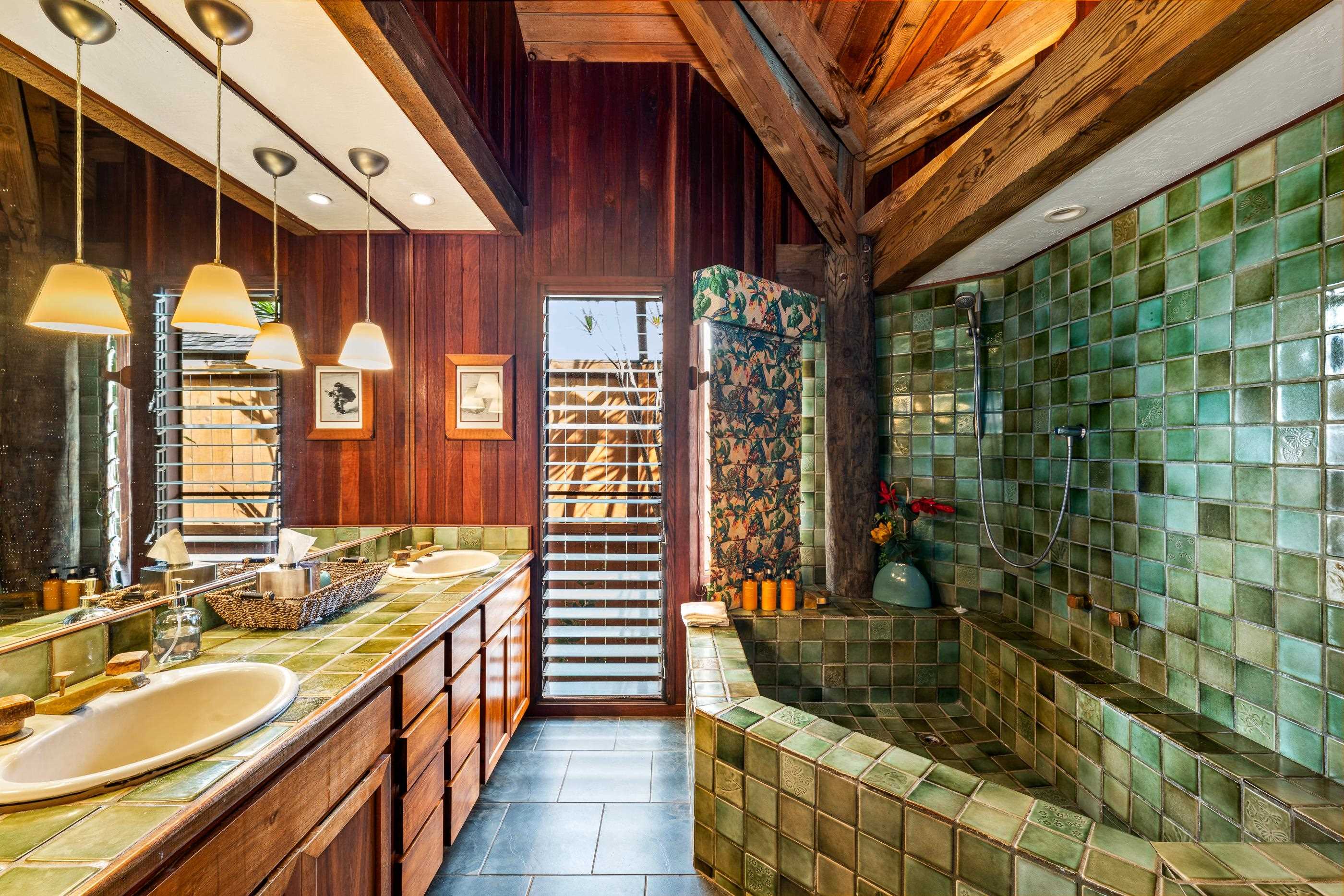 Bathroom with double sinks on green tile, pendant lights and the deep tiled soaking tub
