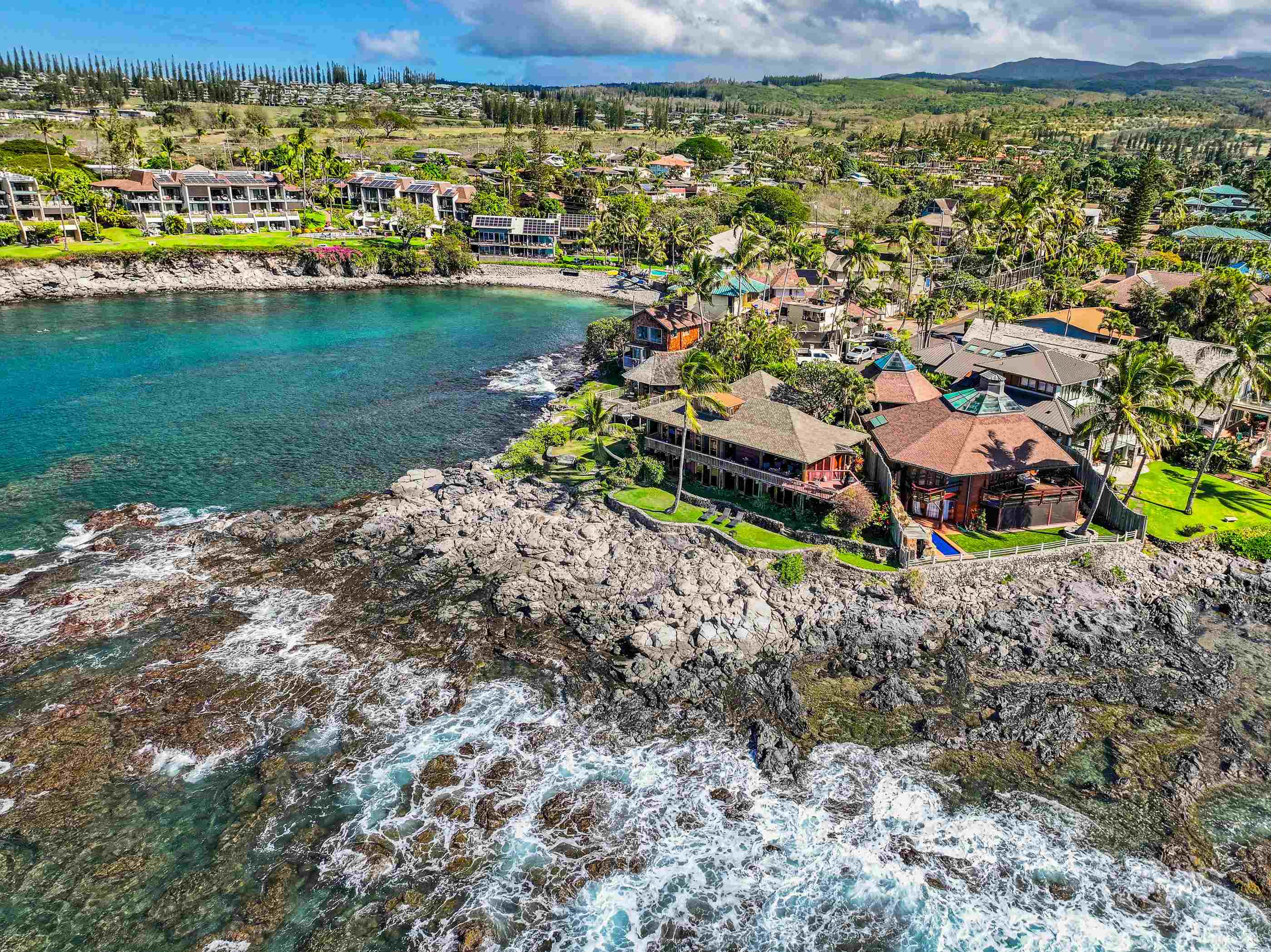 Aerial of the ten-home peninsula, houses ringing the cove above lava rock and turquoise water