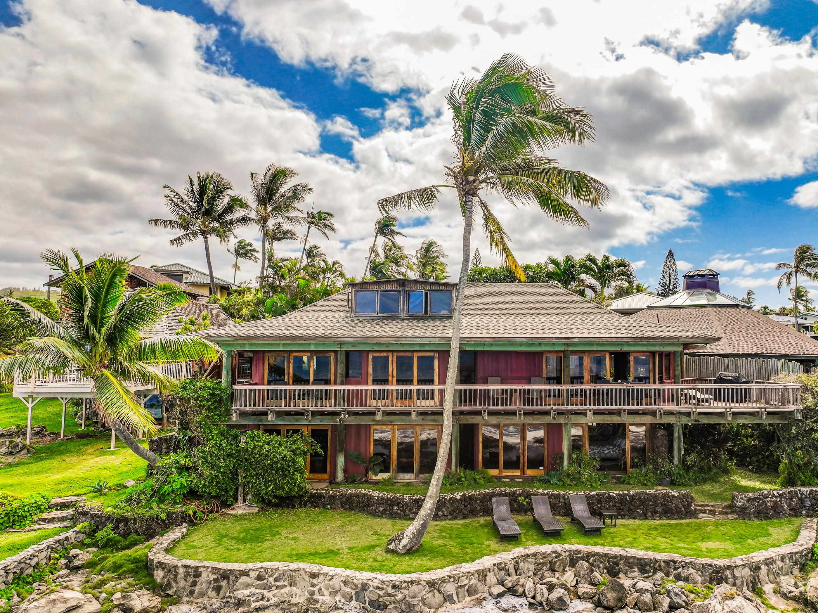 The full two-storey facade from the side lawn, palms overhead and loungers lined up along the rock wall