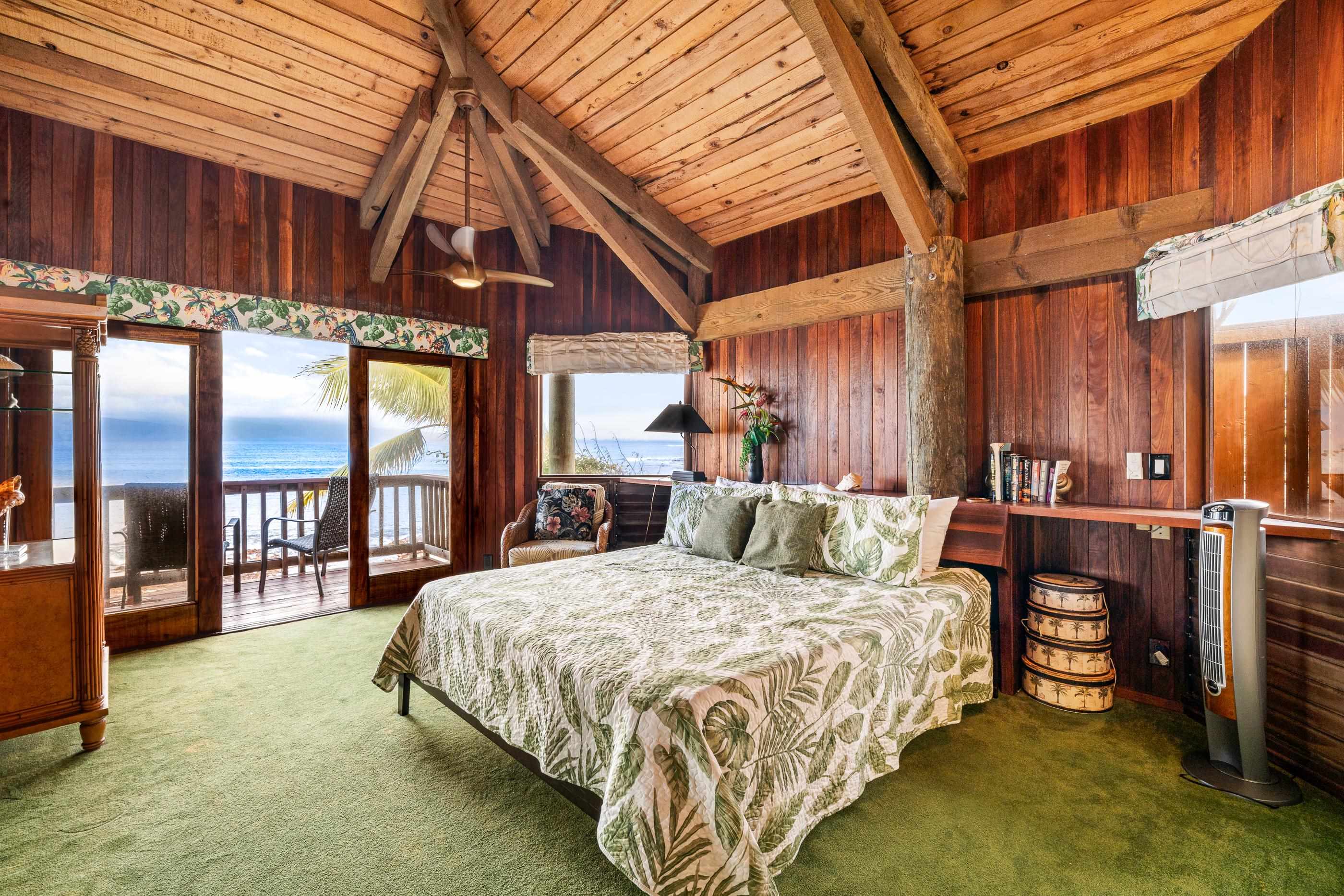 Primary bedroom under vaulted beams, glass doors opening to the deck and the water